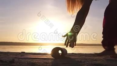 <strong>靠近</strong>一个瑜伽女子展开瑜伽垫在<strong>靠近</strong>水的沙子上。 阳光明媚。 清晨黄昏
